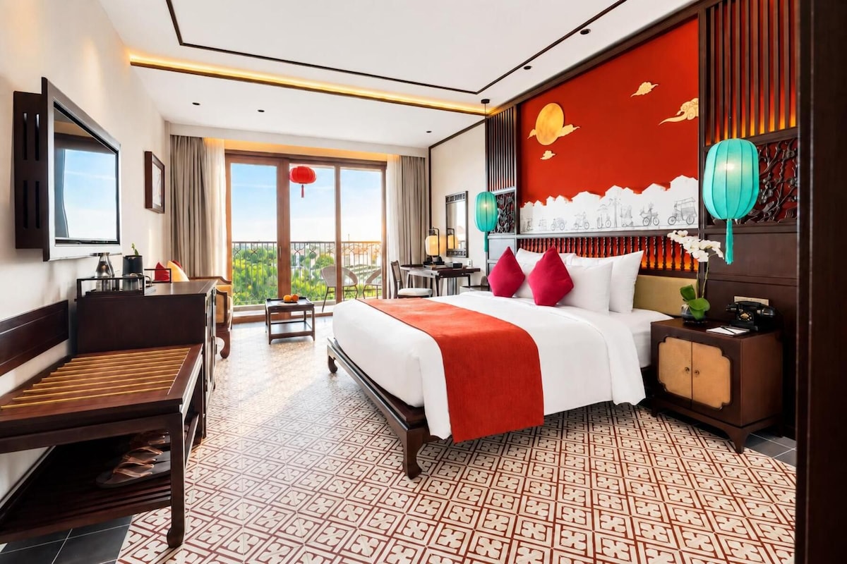 Habitación de hotel con cama, escritorio, silla y balcón con vistas.