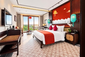 Habitación de hotel con cama, escritorio, silla y balcón con vistas.