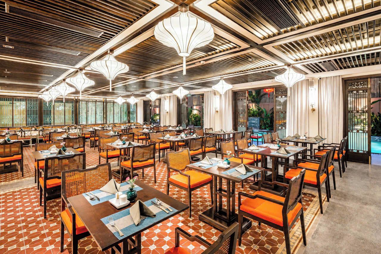 A spacious dining area with multiple tables and chairs, a patterned floor, and a ceiling with hanging light fixtures.