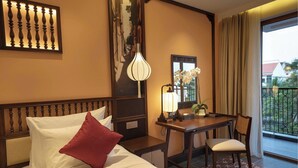 Habitación de hotel con cama, escritorio, silla, espejo y vista al exterior.