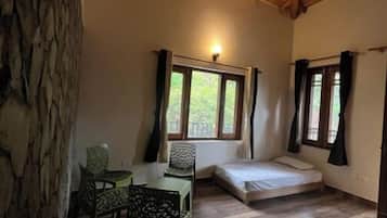 A room with a wooden ceiling, a bed, a table with chairs, and a window with curtains.