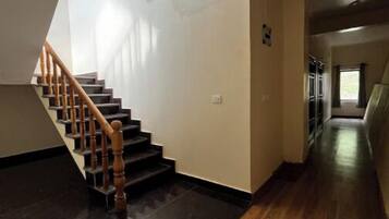A staircase with wooden handrails leading to a landing, a black tiled floor, and a hallway with wooden flooring.