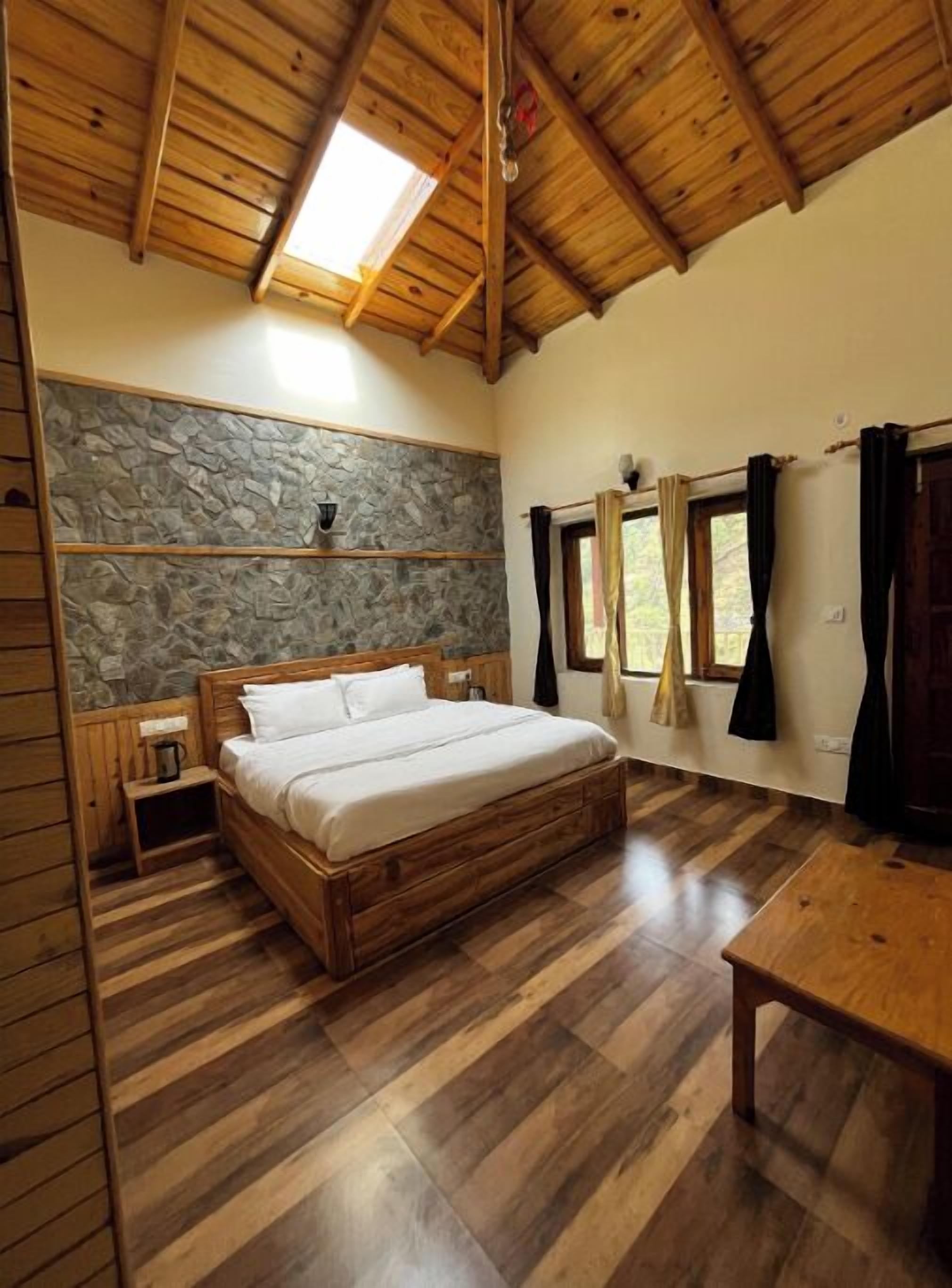 A wooden-framed room with a bed, stone wall, and a window with curtains.