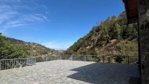 A paved terrace with a metal railing, overlooking a hilly landscape. - Peach Farm Stay (Ramgarh)