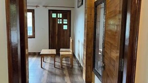 A hallway with wooden flooring, a bench, and a door with a glass panel. - Peach Farm Stay (Ramgarh)