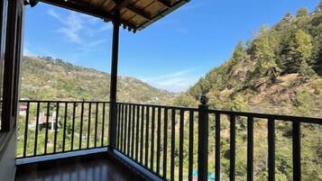 A balcony with a wooden ceiling and black railing, overlooking a mountainous landscape.