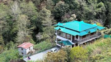 A two-story building with a green roof, surrounded by dense forest.