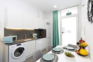 A compact kitchen with a washing machine, microwave, and a dining area with a table set for two. - Guestready - Llovera Apartments (Valencia)