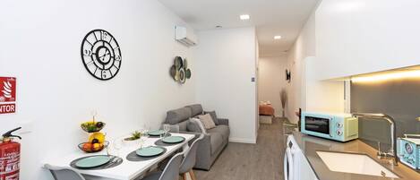 A compact living space with a dining area, kitchenette, and a gray sofa.