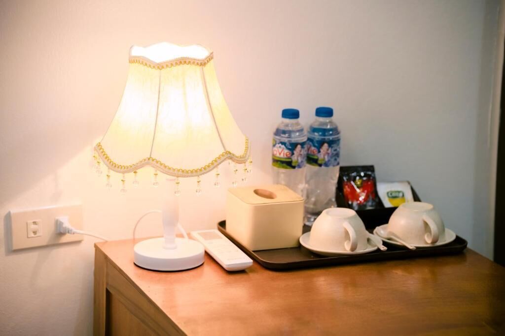 Uma mesa de cabeceira com uma luminária, um estojo de lenços, duas garrafas de água e duas chávenas.