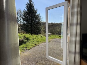 A room with a large glass door leading to a gravel path and a forested hillside. - Gigha - a chalet that sleeps 4 guests in 2 bedrooms (Oban)