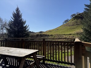 A wooden deck with a table and chairs, overlooking a hilly landscape with trees and a clear sky. - Gigha - a chalet that sleeps 4 guests in 2 bedrooms (Oban)
