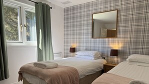 Hotellihuone, jossa on kaksi sänkyä, ikkuna, jossa on verhot, peili ja seinä, jossa on ruutukuviota.