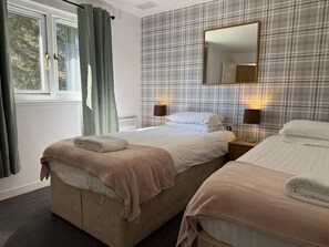 A hotel room with two beds, a window with curtains, a mirror, and a wall with a plaid pattern. - Gigha - a chalet that sleeps 4 guests in 2 bedrooms (Oban)