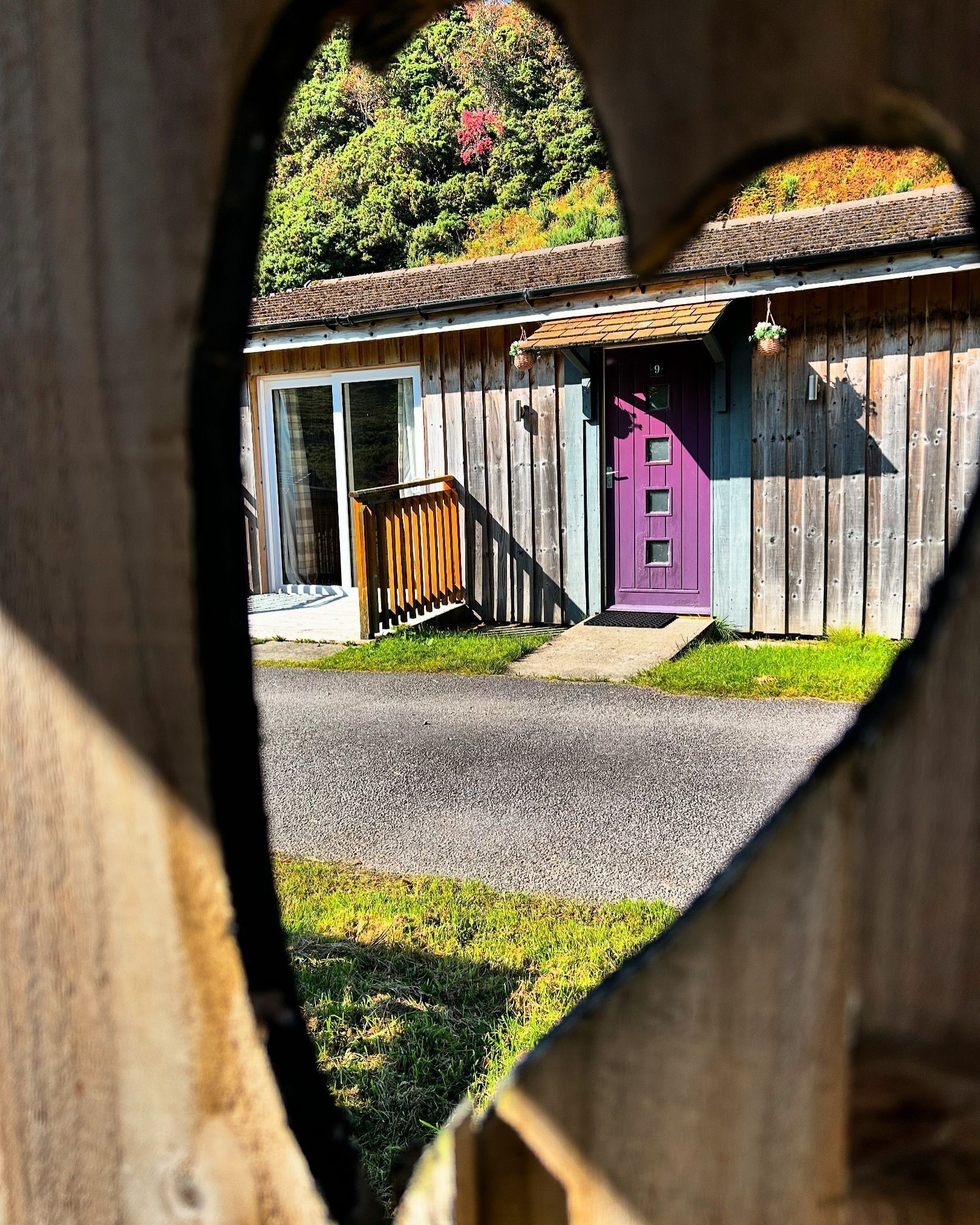A wooden building with a purple door and a number 9 sign, viewed through a heart-shaped cutout.