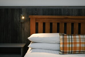 Ein Bett mit hölzernem Kopfteil, weißen Kissen und einem karierten Kissen.