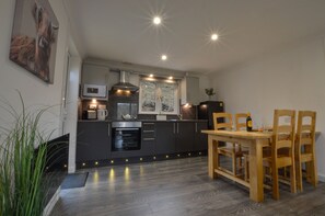 Eine moderne Küche mit dunklen Schränken, einem Holztisch und Einbauleuchten.