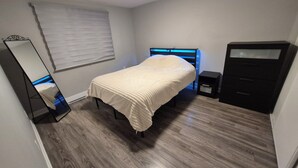 A bedroom with a bed, a dresser, a mirror, and a window with blinds.