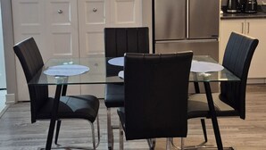 A modern kitchen with a glass dining table, black chairs, a stainless steel refrigerator, and a microwave.