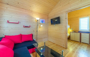Ein gemütliches Blockhaus-Interieur mit einer Couch, einem Glastisch, einem Fernseher und einer Küchenzeile.