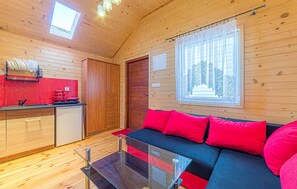 Ein gemütliches Blockhäuschen-Interieur mit einer Küchenzeile, einem Glastisch und einem roten Sofa.