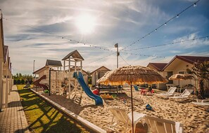 Ein Strandresort mit Spielplatz, Reetdachschirmen und Liegestühlen.