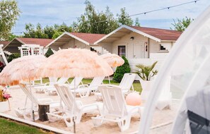 Liegestühle im Freien, ein Strandsonnenschirm und ein Gebäude mit rotem Dach.