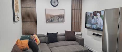 A modern living room with a sectional sofa, a flat-screen TV, and a built-in refrigerator.