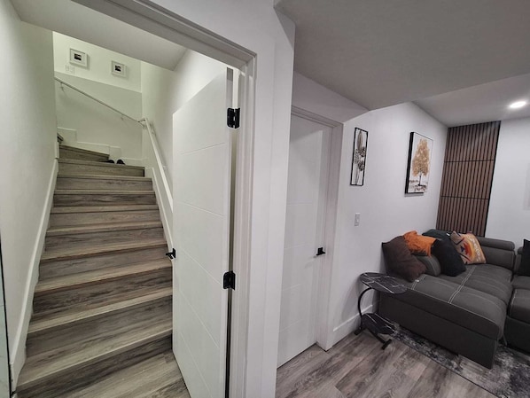 A staircase leading to a landing with a white door, a gray sofa with cushions, and two framed artworks on the wall.