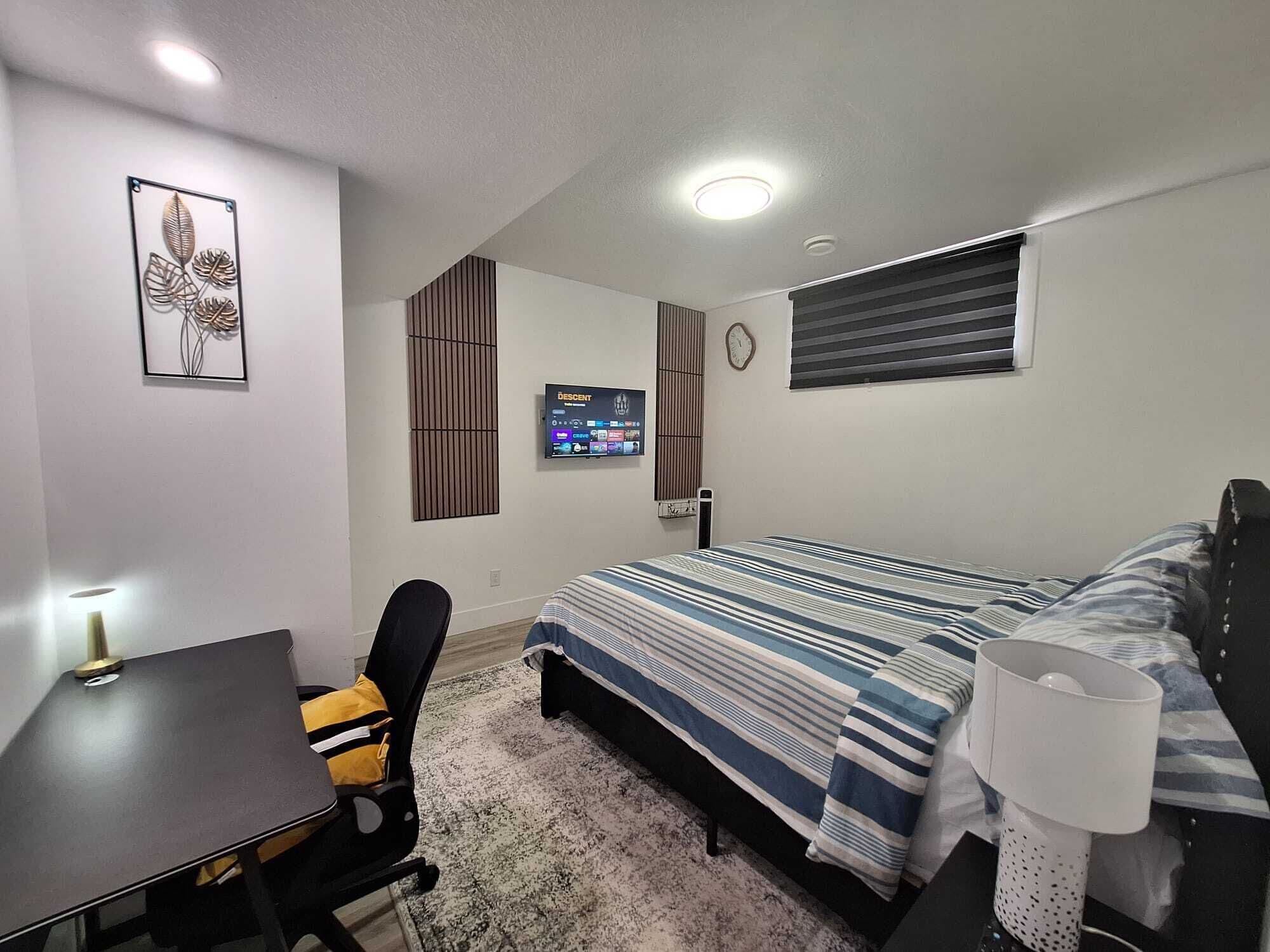 A bedroom with a bed, a desk, a chair, a TV, and a clock on the wall.