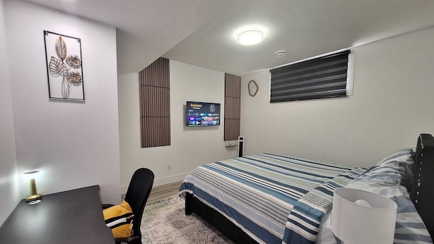 Un dormitorio con cama, escritorio, silla, televisor y un reloj en la pared.