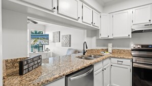 A modern kitchen with white cabinets, granite countertops, stainless steel appliances, and a view of a marina.