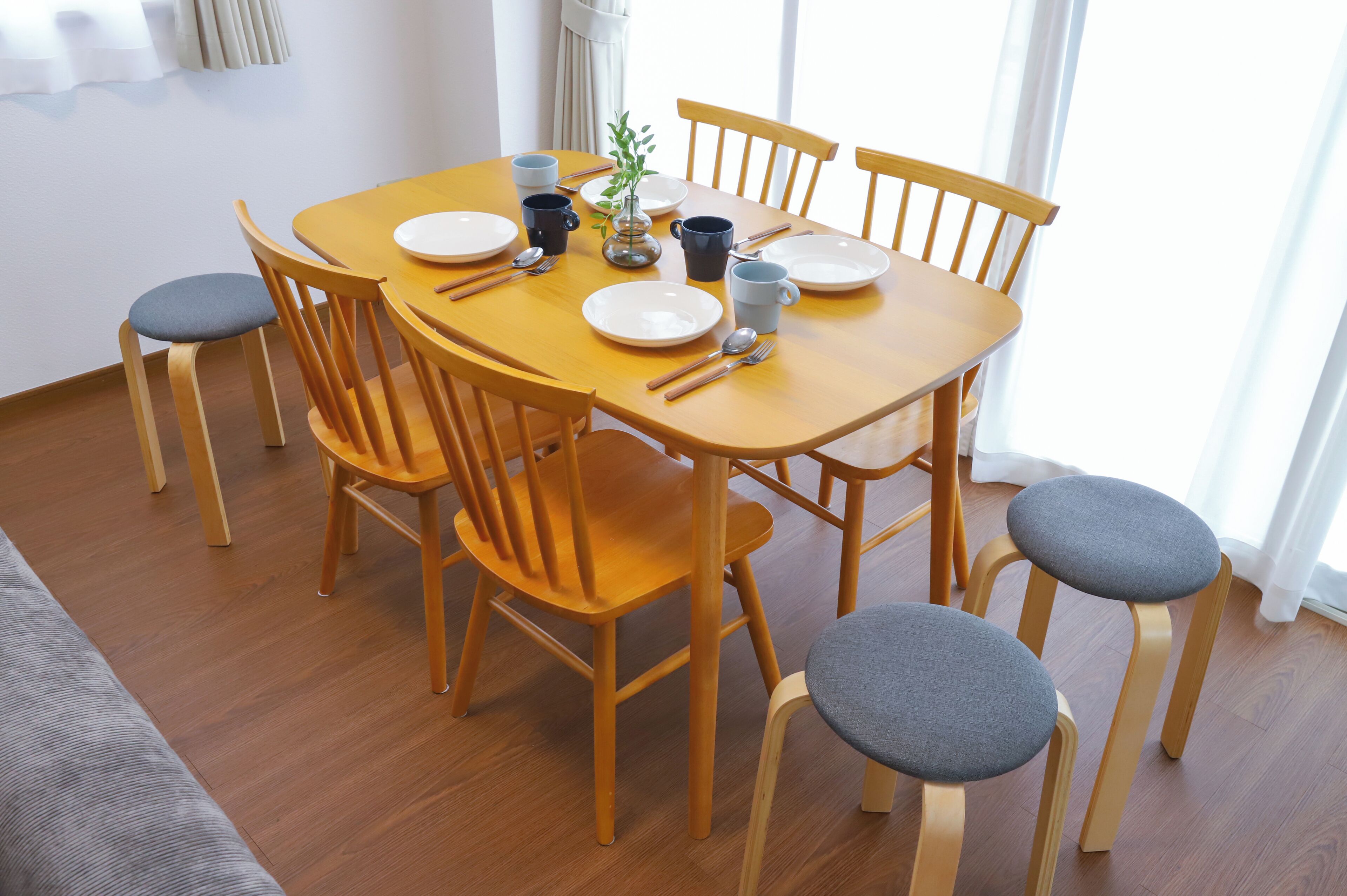 A dining table set with plates, cups, and cutlery, surrounded by wooden chairs with grey cushions.