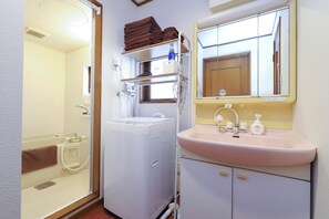 A compact bathroom with a white washing machine, a sink with a mirror above, and a shower area. - 3-Bedroom House, Near Ikebukuro and a Shopping Arcade (Nukui, Nerima City)