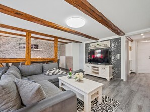 Ein Wohnzimmer mit Ecksofa, Flachbildfernseher, Holzboden und Backsteinwand.