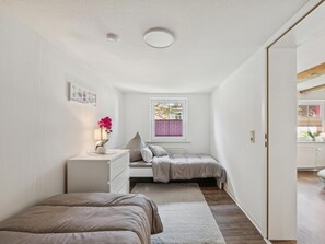 Ein Schlafzimmer mit Bett, Nachttisch mit Lampe, Fenster mit Jalousien und einer Tür zu einem anderen Raum.
