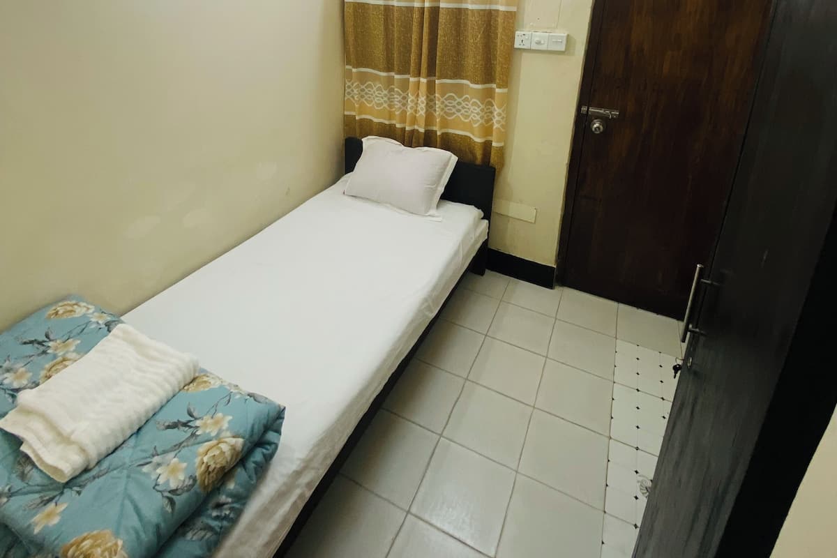 A small, single-bed room with a ceiling fan, a wooden door, and a curtain.