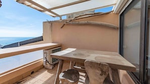 Uma varanda com mesa de madeira, uma cadeira e vista para o mar.