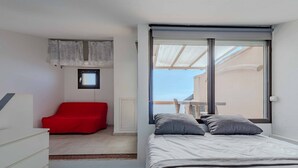 Quarto com cama, uma cadeira vermelha, uma janela pequena e vista para o exterior.