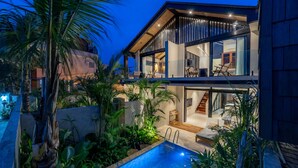 Uma casa moderna de dois andares com piscina, mobiliário para área externa e plantas tropicais.