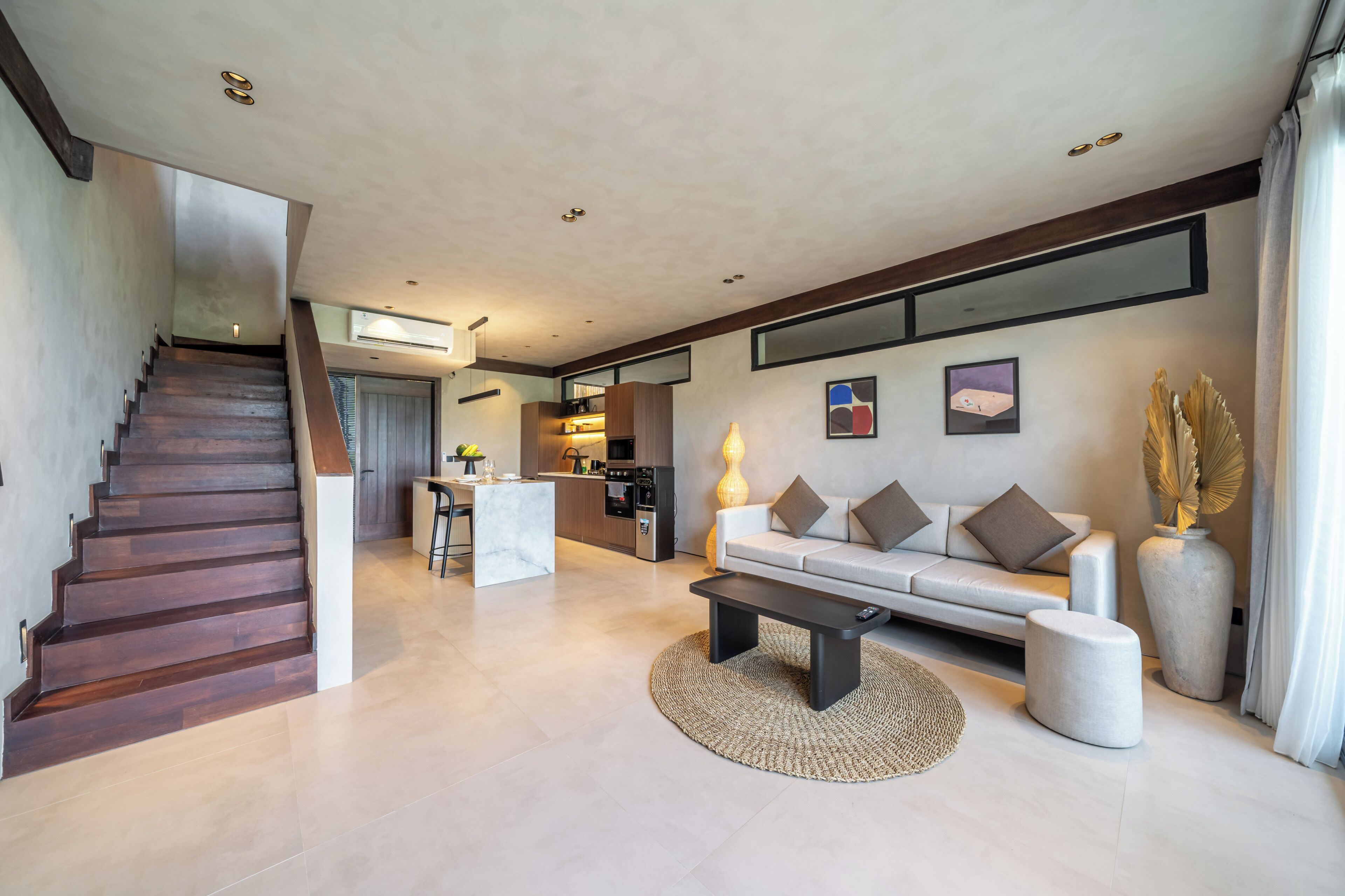 A modern living room with a staircase, a sofa, a coffee table, and a kitchen area in the background.