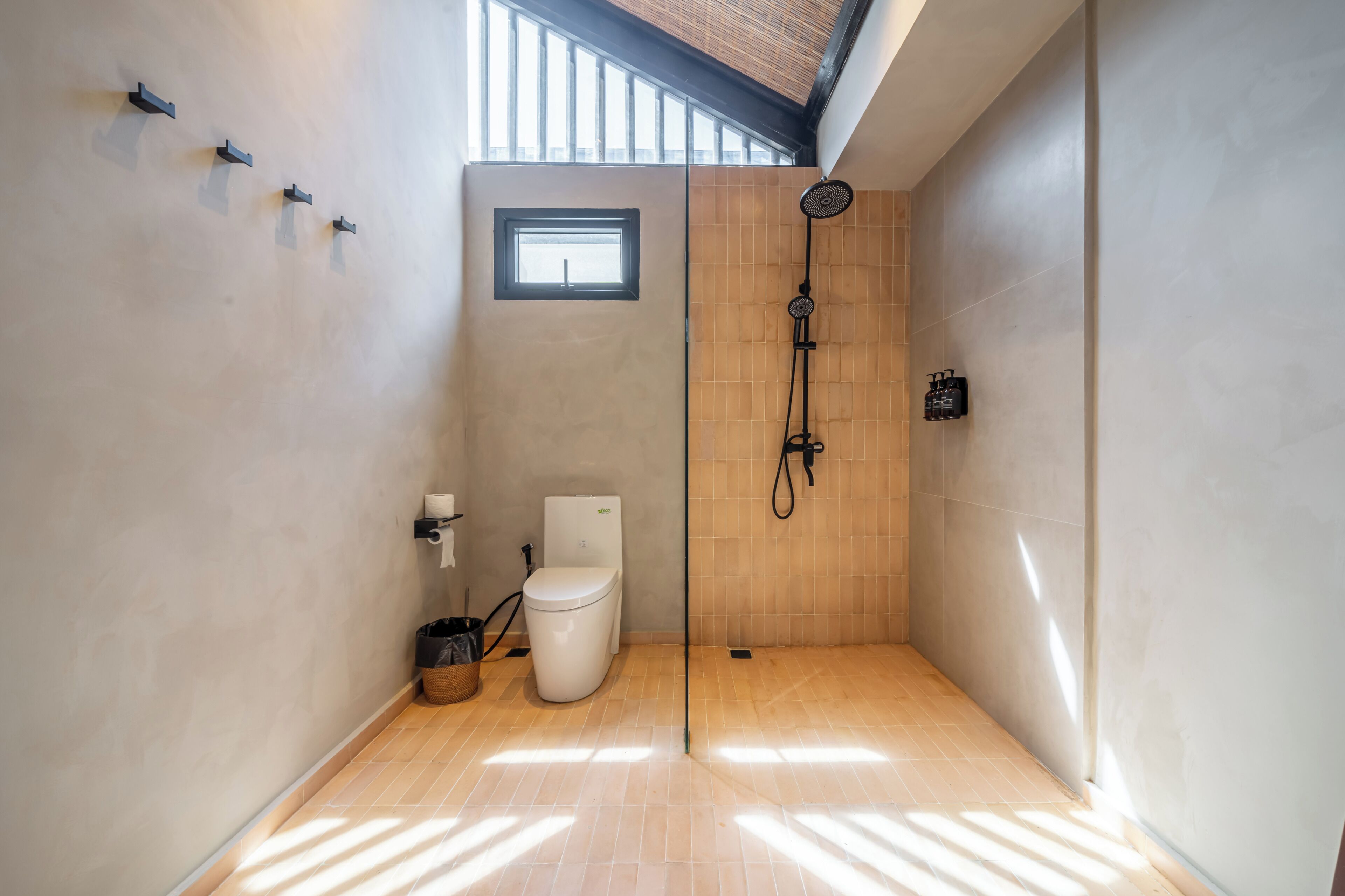 A modern bathroom with a toilet, shower, and a small window.