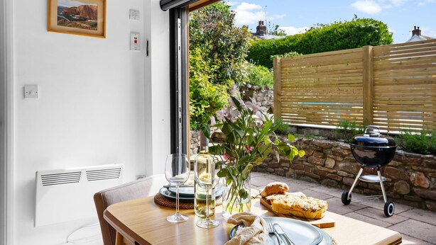 A dining table with a glass of wine, a vase with flowers, and a loaf of bread. - The Granary - Swimming pool, Parking, Garden, BBQ (Georgeham)