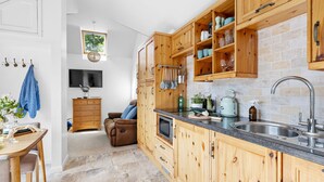 A modern kitchen with wooden cabinets, a built-in stove, and a large window. - The Granary - Swimming pool, Parking, Garden, BBQ (Georgeham)