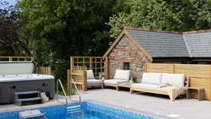 A pool area with a hot tub, wooden deck, and stone building. - The Granary - Swimming pool, Parking, Garden, BBQ (Georgeham)