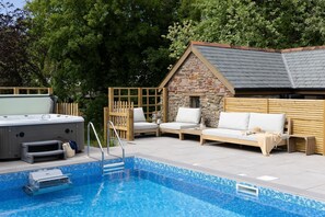Ein Poolbereich mit Whirlpool, Holzterrasse und Steinhaus.