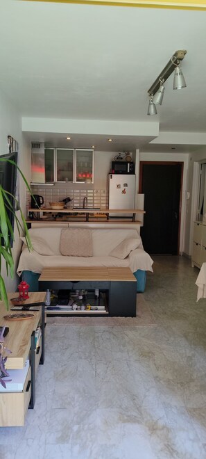 Ein modernes Wohnzimmer mit Sofa, Couchtisch, Fernseher und einer Küchenzeile im Hintergrund.