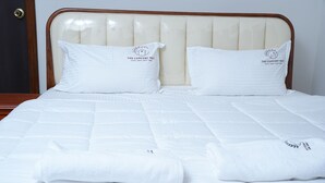 Una cama bien hecha con cabecera, dos almohadas con un logotipo y toallas dobladas.