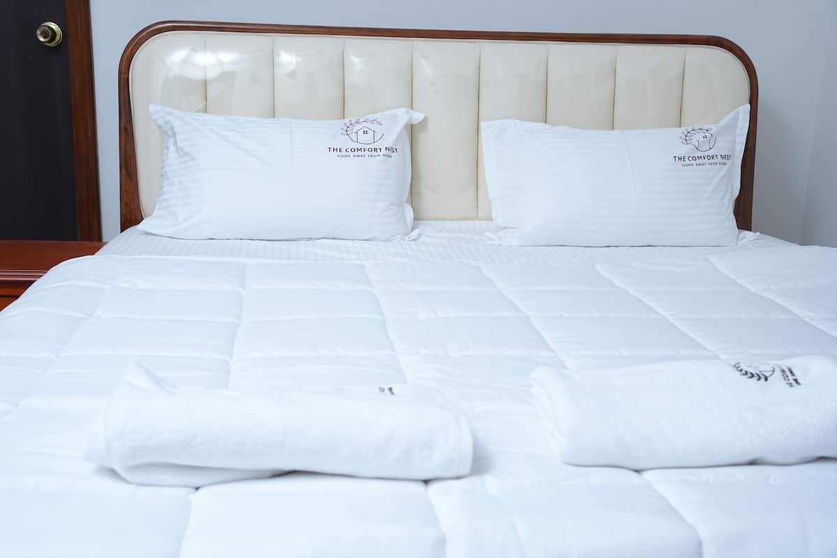 A neatly made bed with a headboard, two pillows with a logo, and folded towels.