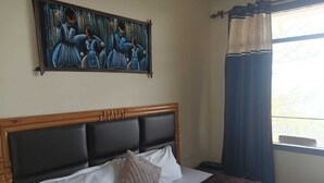 A bed with a wooden headboard, white and beige pillows, a dark brown blanket, and a painting above the bed. - Pankaj Homestay (Shimla)